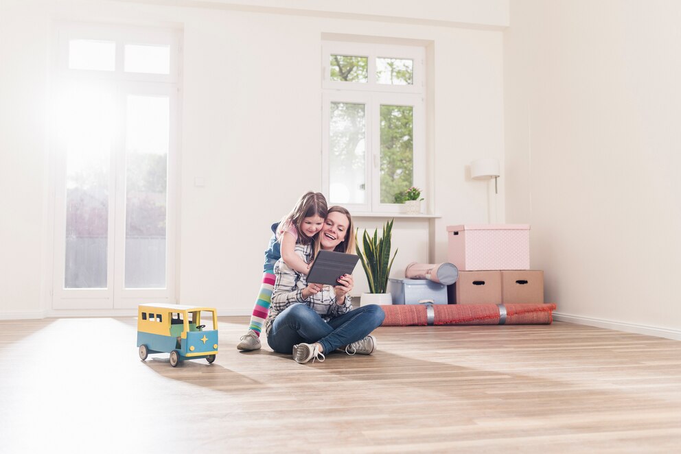 Mutter sitzt am Boden und wird von ihrem Kind umarmt. Gemeinsam planen sie die Einrichtung des Kinderzimmers.