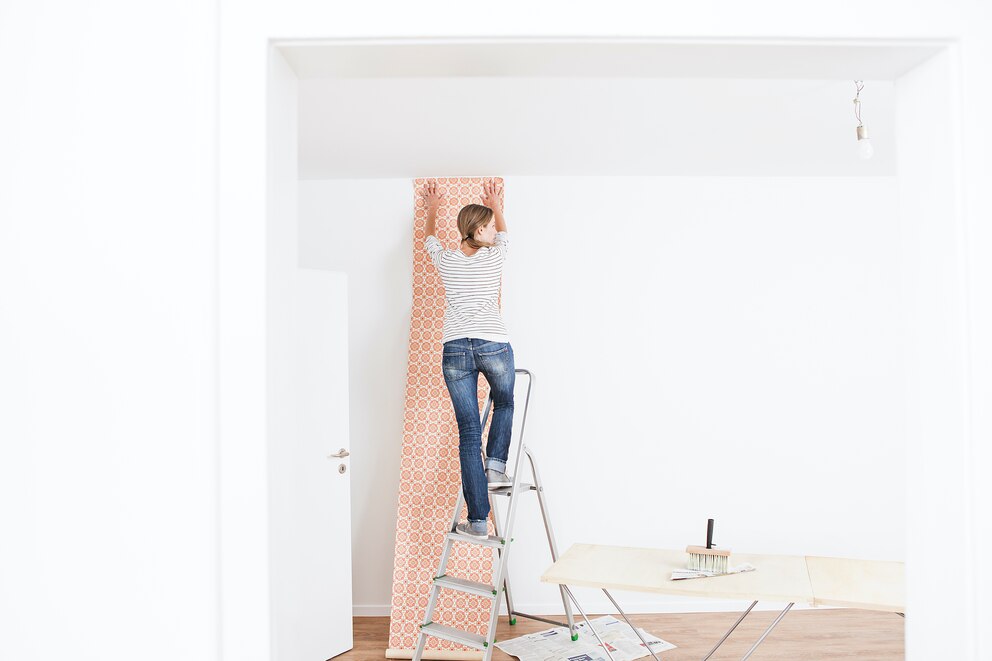 Frau, die eine Tapetenbahn an der Wand anbringt und wartet bis diese haftet