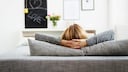 Frau, die gemütlich auf einem Sofa sitzt und die gegenüberliegende Wand betrachtet