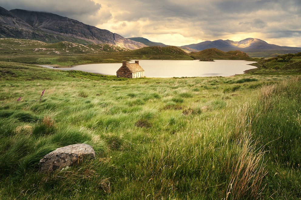 Grüne Naturlandschaft Schottlands mit Haus und See im Hintergrund