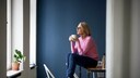 Eine Frau sitzt auf dem Tisch, im Hintergrund ist eine dunkelblaue Wand zu sehen.