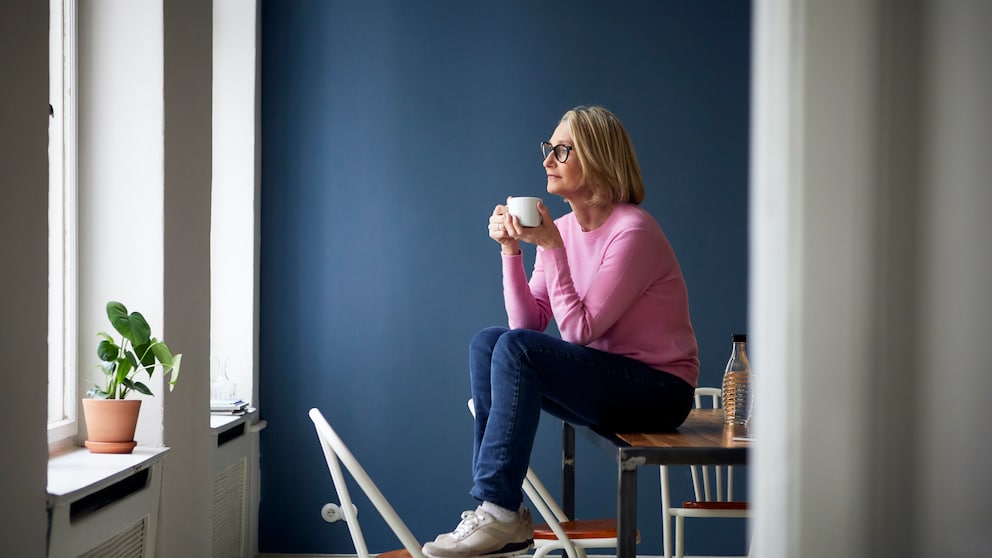 Eine Frau sitzt auf dem Tisch, im Hintergrund ist eine dunkelblaue Wand zu sehen.