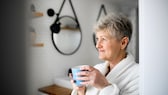 Frau mit einer Tasse Kaffee in der Hand im Badezimmer