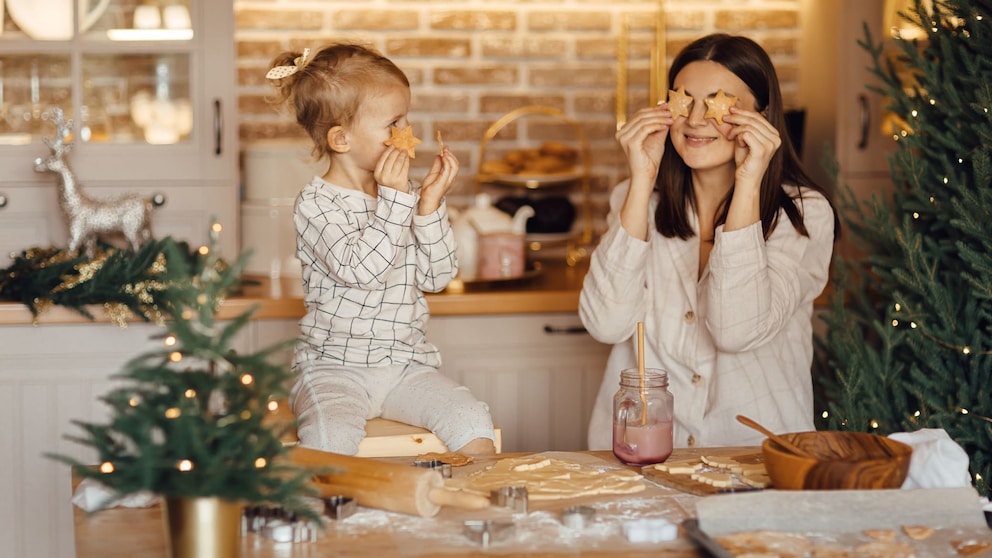 Plätzchen backen mit Kindern: Eine Mama hält sich Plätzchen vor das gesicht. Ihre Tochter macht es nach.