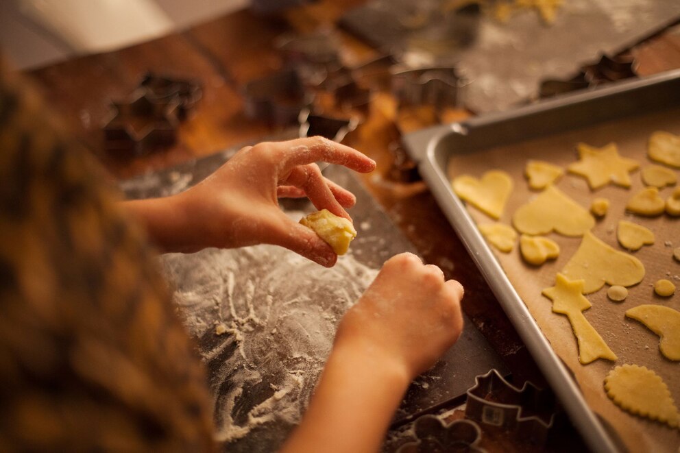 Kind hat teig in den Händen. Vor ihr liegt ein Blech mit ausgestochenen Plätzchen