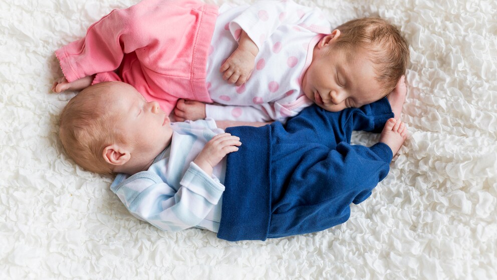 Mädchen Rosa: zwei Babys aneinandergeschlungen mit rosafarbener und blauer Hose