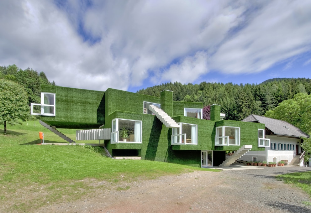 Bauernhaus: Ein Neubau mit Kunstrasen an der fassade, daneben ein Bauernhaus