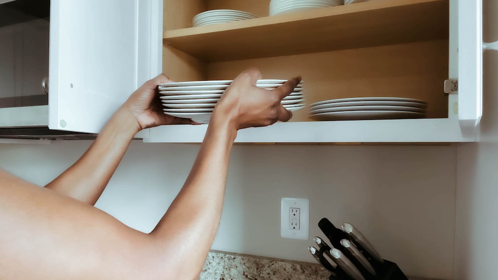 Nahaufnahme einer nicht erkennbaren Frau, die sauberes Geschirr auf ein Regal im Küchenschrank stellt