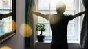Person zieht Vorhänge am Fenster beiseite