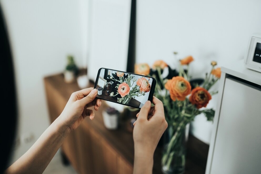 Person, die mit dem Smartphone einen Strauß Blumen im Interieur fotografiert