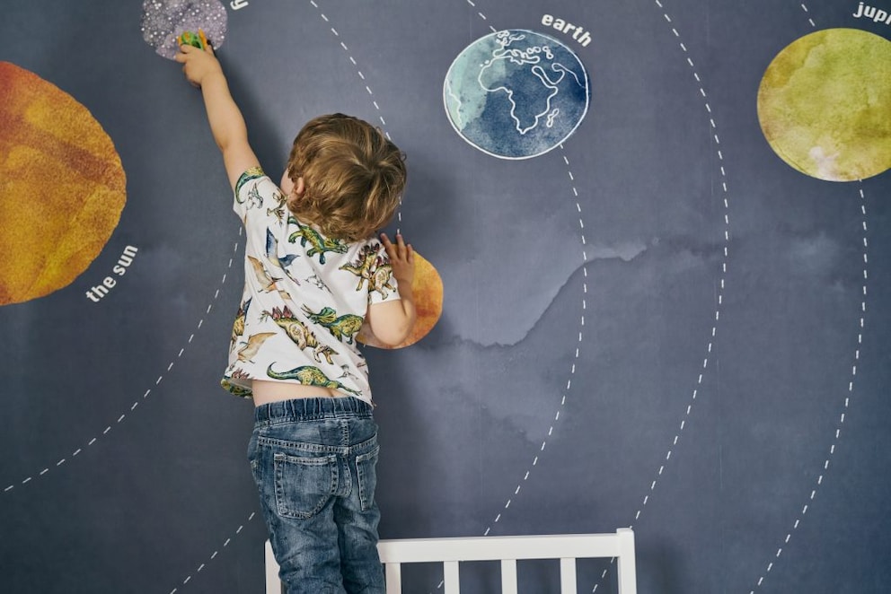 Boy pointing at the solar system on the wall in his room