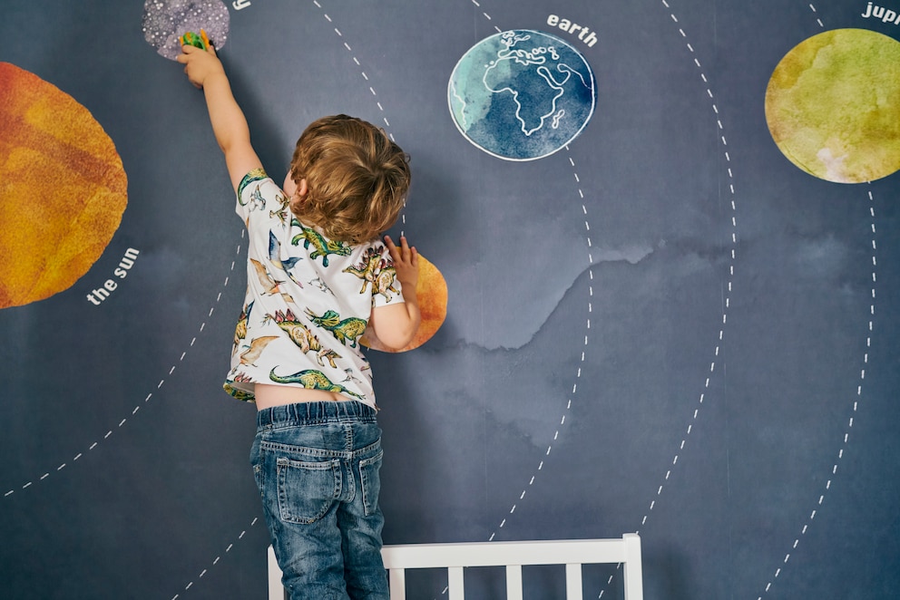 Junge zeigt auf das Sonnensystem auf der Wand in seinem Kinderzimmer