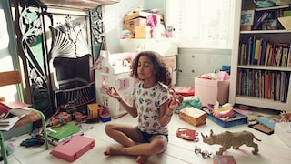 Kleines Mädchen, das scheinbar mitten im Kinderzimmerchaos meditiert