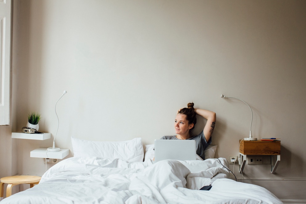 Junge Frau, die mit ihrem Laptop im Bett liegt