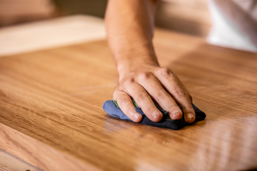 Person, die mit einem Tuch das Pflegeöl ins Holz einarbeitet