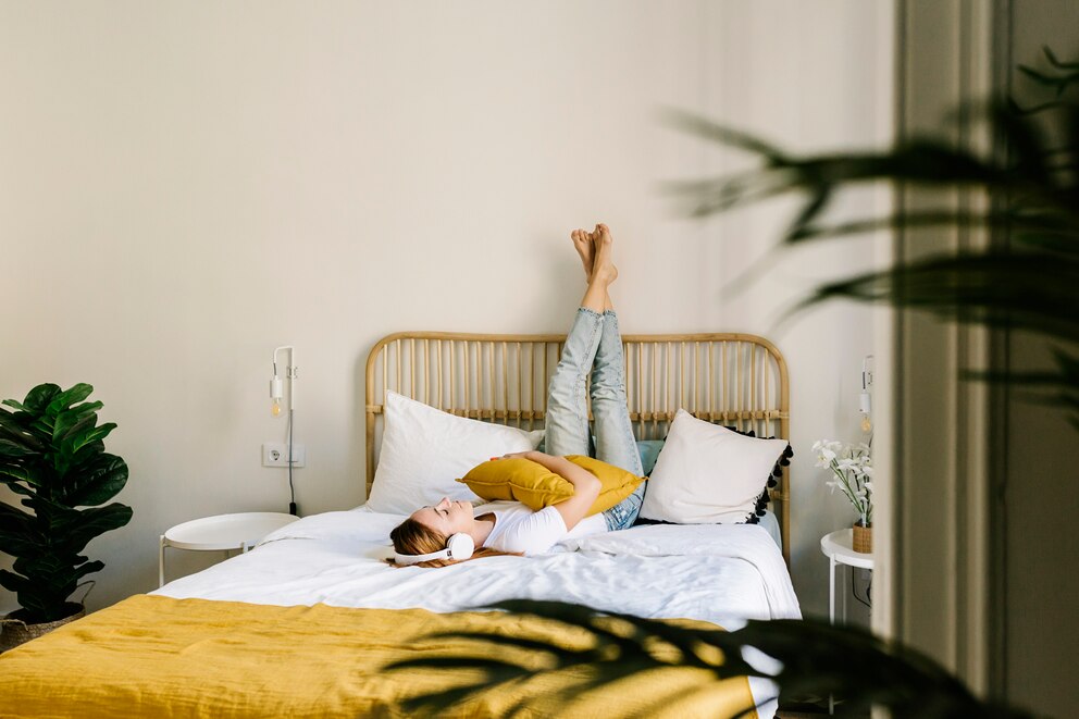 Eine Person liegt auf dem Bett, welches mit einem KIssen und einer Decke in Gelb ausgestattet ist