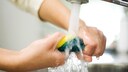 Spülschwamm: Mann wringt Spülschwamm unter laufendem Wasserhahn aus