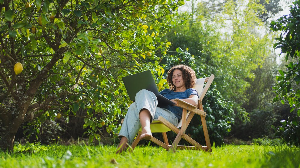 Frau sitzt mit Laptop im Garten