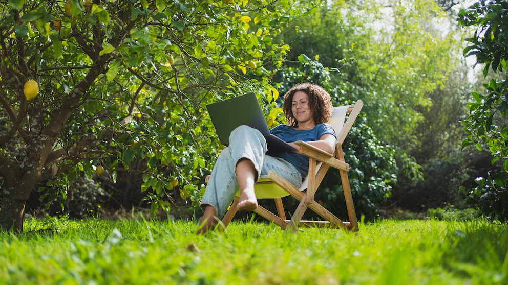 Frau sitzt mit Laptop im Garten