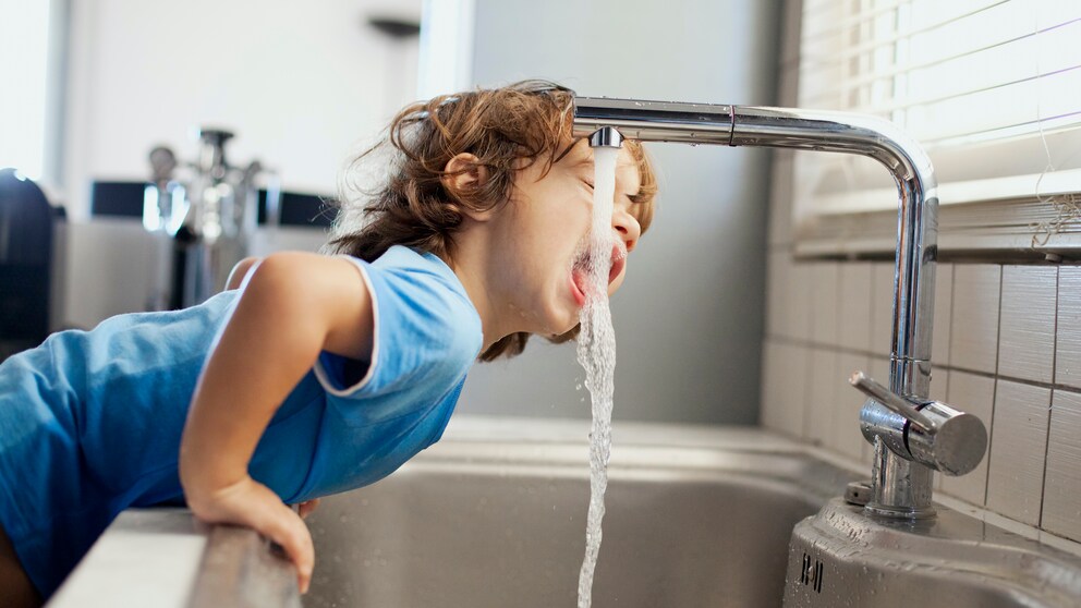 Junge trinkt aus einem Wasserhahn