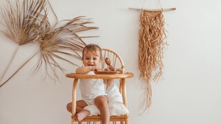 Kleinkind, das in seinem Stühlchen sitzt, in einem nachhaltig eingerichteten Kinderzimmer