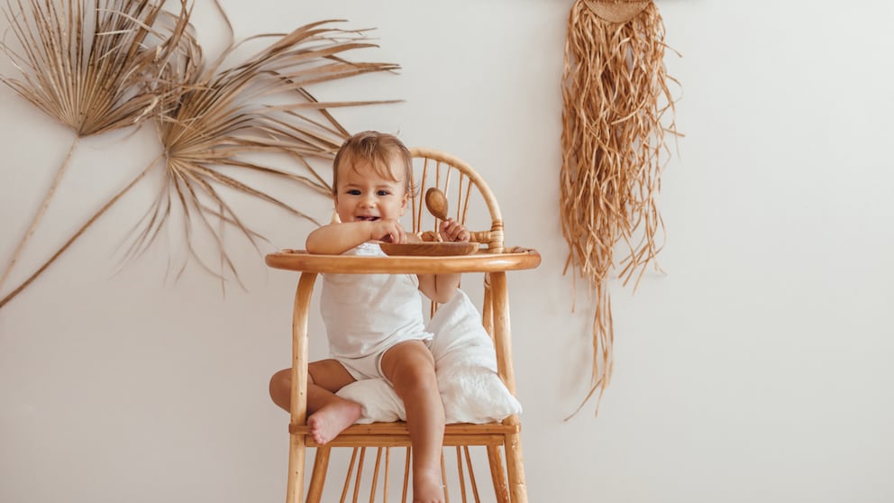 Kleinkind, das in seinem Stühlchen sitzt, in einem nachhaltig eingerichteten Kinderzimmer