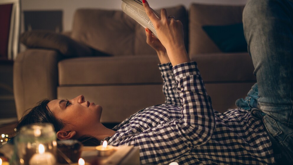 Frau liegt auf dem Boden und liest bei Kerzenschein ein Buch