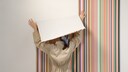 Frau bringt Tapete mit buntem Streifen-Muster an der Wand an
