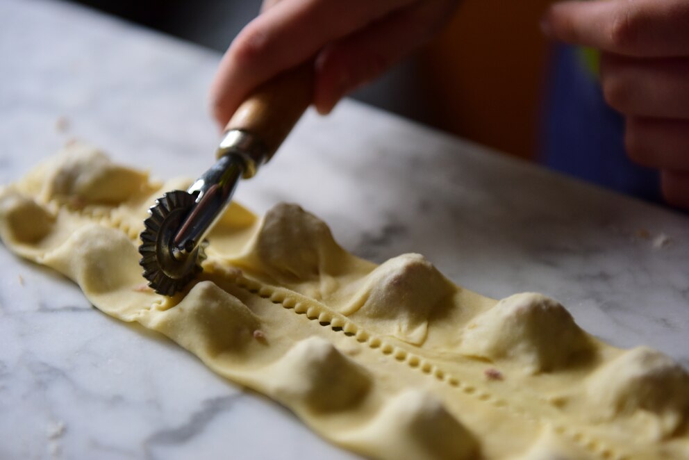 Person, die Tortellini auf einer Arbeitsplatte aus Naturstein vorbereitet