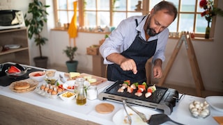 Mann bereitet Gemüse und Fleisch auf einem Elektrogrill bzw. Tischgrill vor.