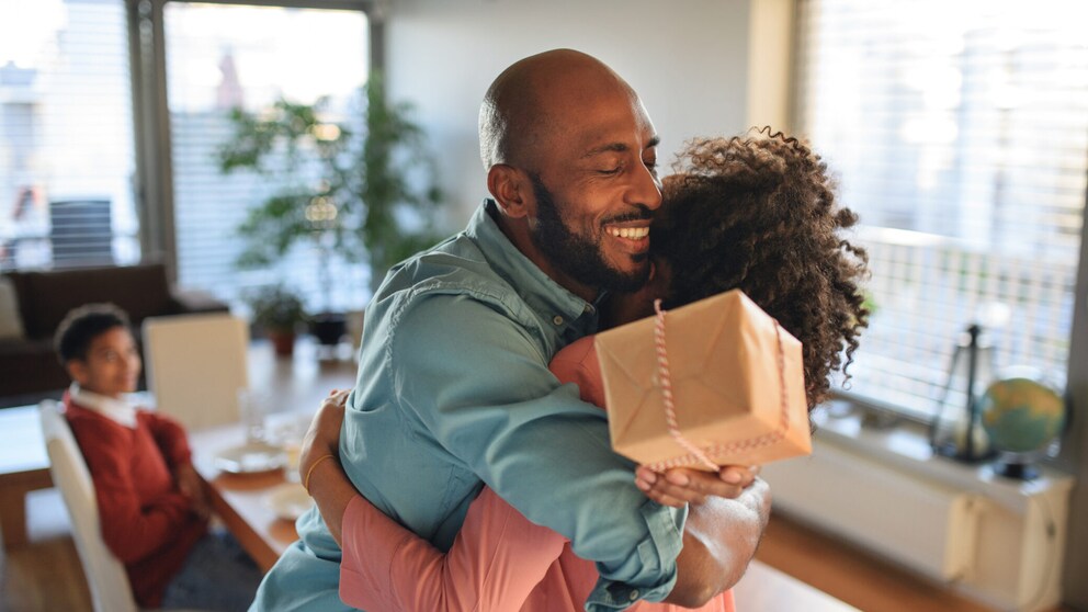 Vater umarmt Kind mit Geschenk in der Hand.