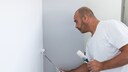Maler, der eine Raumecke mit kleiner Walze und Pinsel streicht