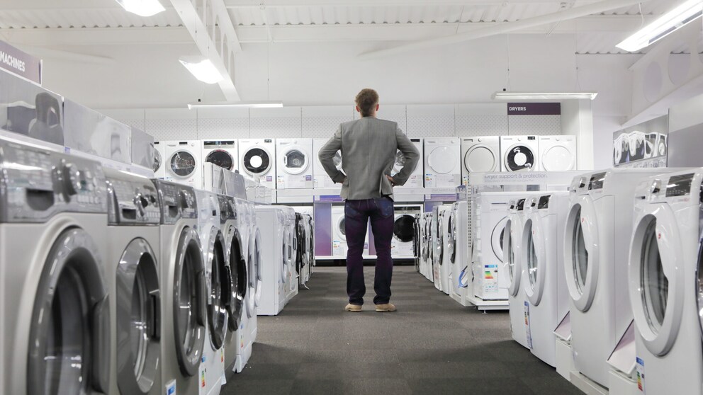 Mann steht vor vielen Waschmaschinen beim Einkaufen.