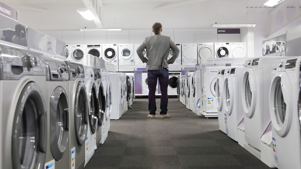 Mann steht vor vielen Waschmaschinen beim Einkaufen.