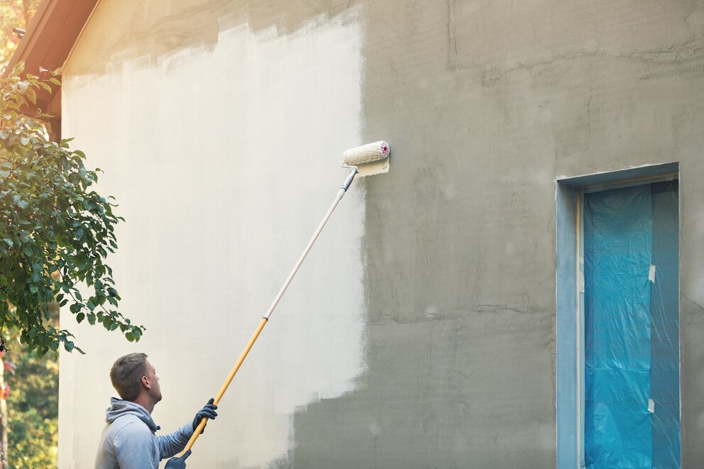 Mann streicht Hausfassade mit neuer Farbe an