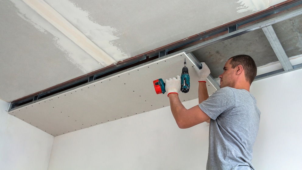 Mann bringt Gipskartonplatten an der Decke an