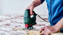 Mann sägt mit einer Stichsäge in der Hand ein Stück Holz