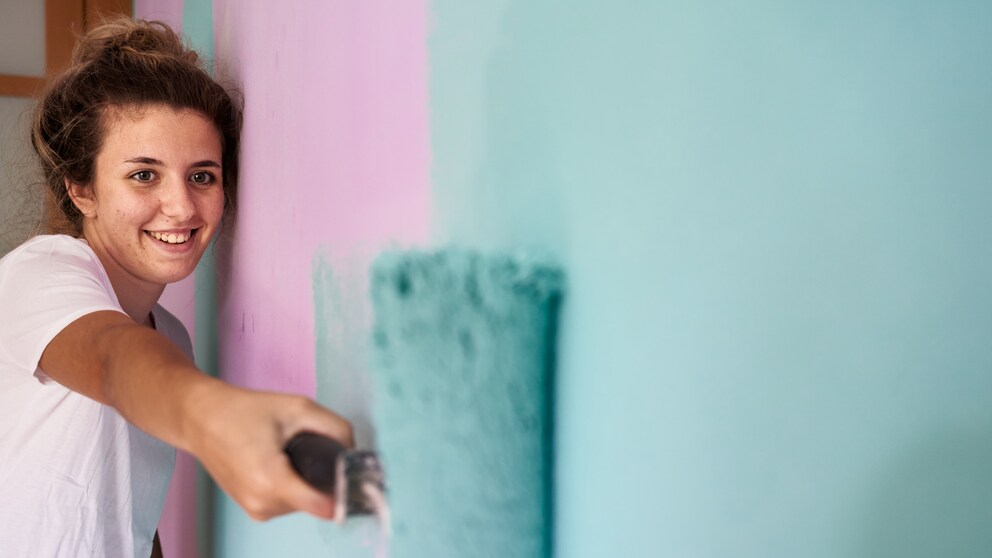 Junge Frau streicht ihre Wand mit Dispersionsfarbe bunt