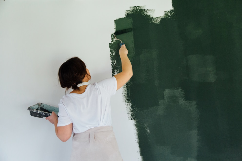 Frau streicht gerade eine Wand in dunklem Grün