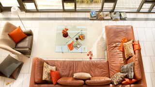 Wohnzimmer mit braunem Ledersofa und orangenen Kissen