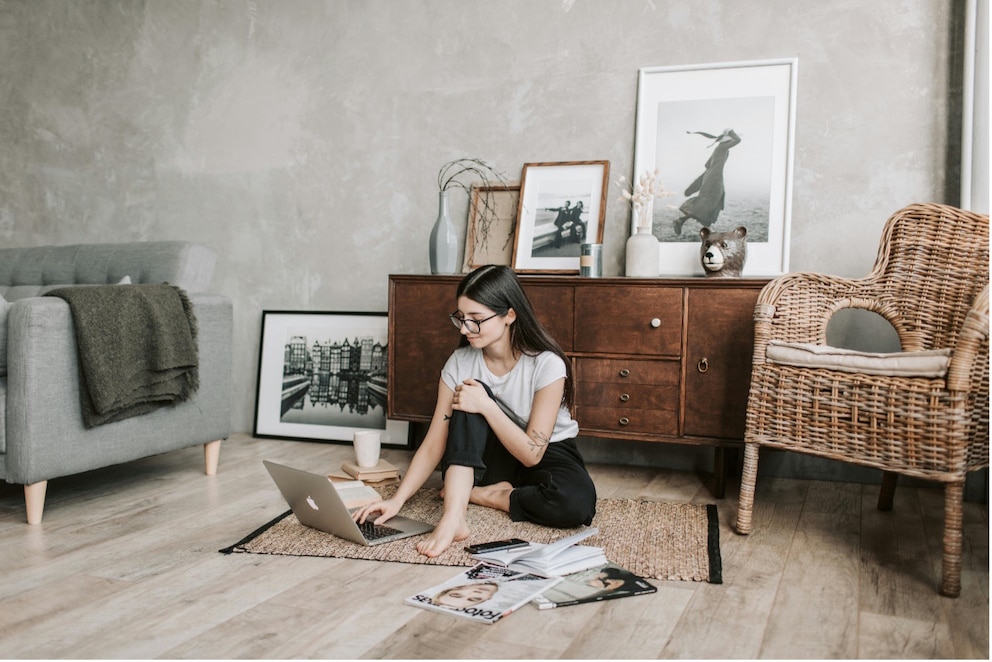 Eine Frau arbeitet mit ihrem Laptop auf dem Boden eines stilvollen Wohnzimmers.