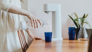 Frau mit Flasche und Wassersprudler auf dem Tisch