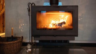 Eine verrußte Glasscheibe am Kaminofen schränkt den Blick auf das lodernde Feuer ein