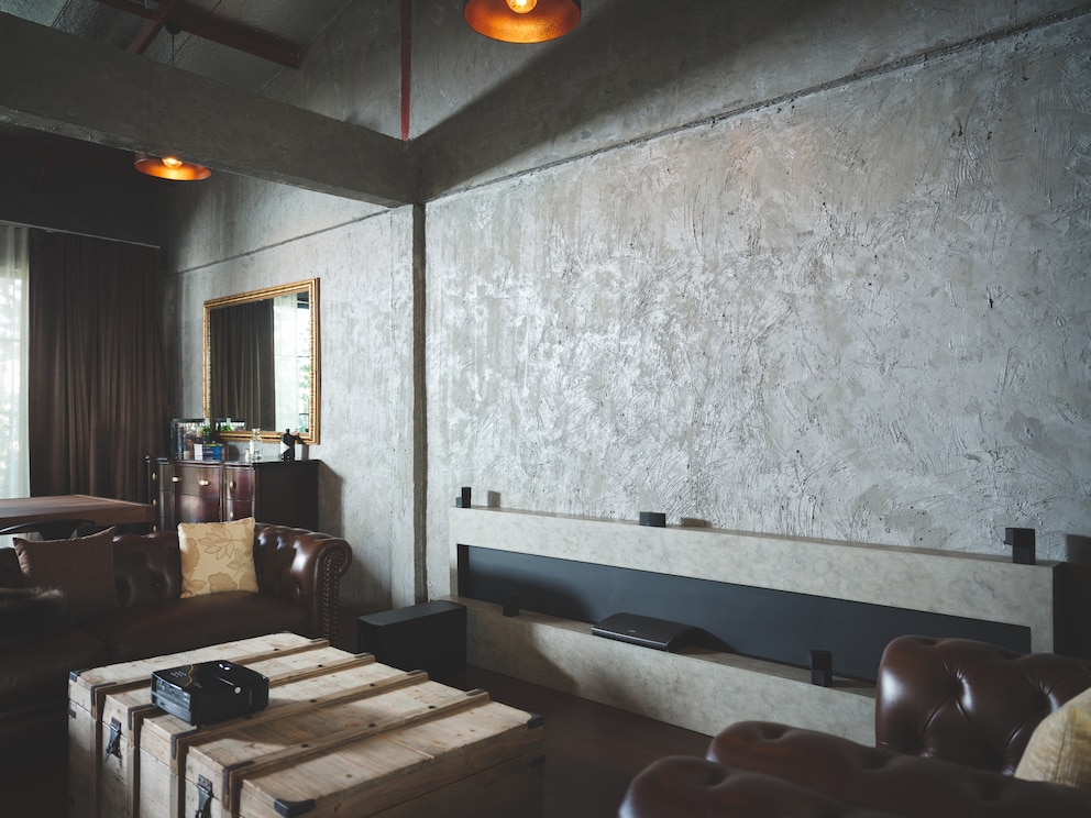 Dunkles industrielles Loft-Interieur mit Ledersofa, Holzkiste und strukturierter Betonwand im "Soft Brutalism " gestaltet.