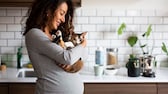 Eine schwangere Frau hält ein Kitten auf dem Arm