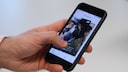 Ein Mann wischt mit seinem Daumen ein Foto in der App „Find Us“, Tiere aus dem Tierheim nach Tinder-Prinzip, beiseite.
