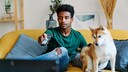 Junger Mann sitzt mit Hund auf dem Sofa vor dem Fernseher