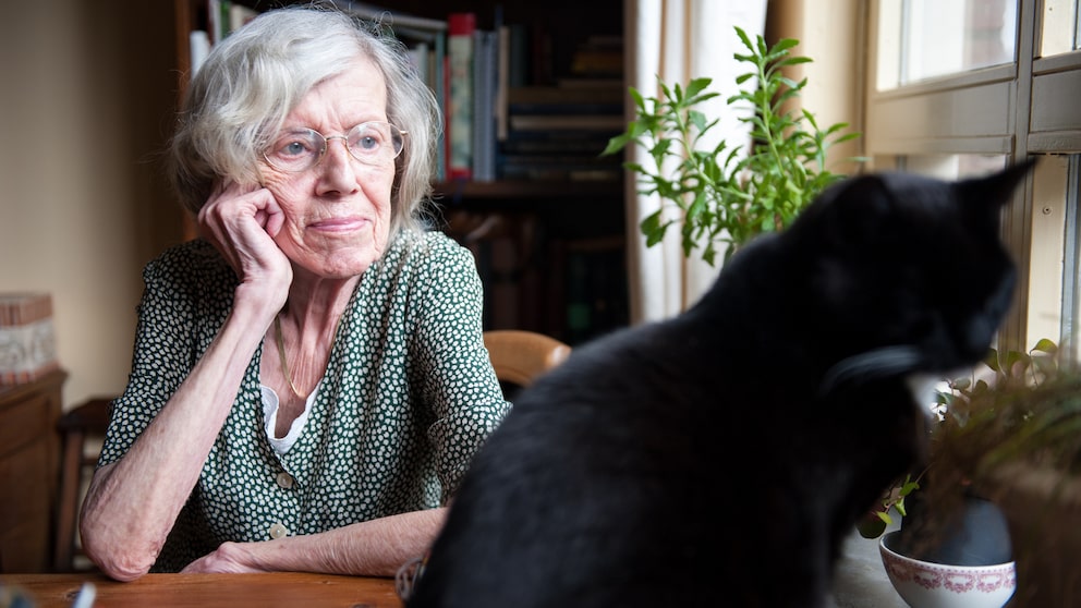 Eine ältere Frau sitzt mit ihrer Katze am Fenster