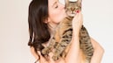 Junge Frau hält eine Katze auf dem Arm und gibt ihr einen Kuss