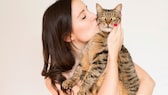 Junge Frau hält eine Katze auf dem Arm und gibt ihr einen Kuss
